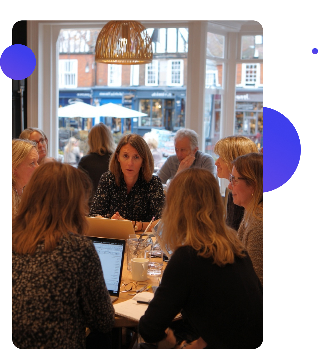 A group of social care professionals meeting around a wooden table with laptops open, talking and smiling in a bright office.