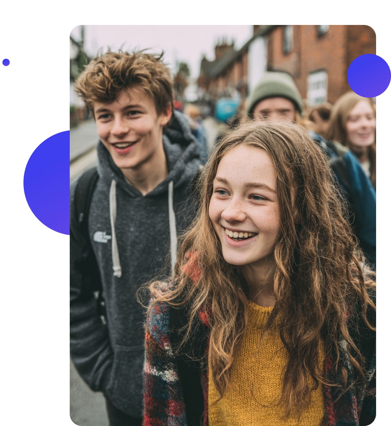 A group of teenagers walking through a UK town, smiling and chatting together, dressed casually on a cloudy day.